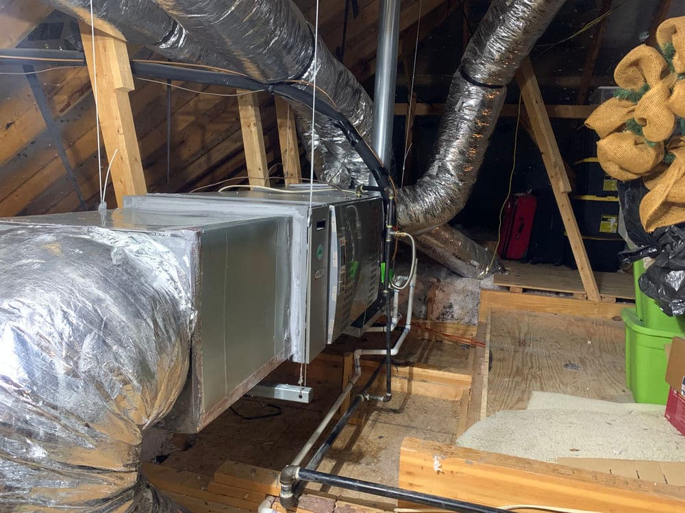 Air conditioning unit and ductwork in a framed attic space with insulation and storage items.