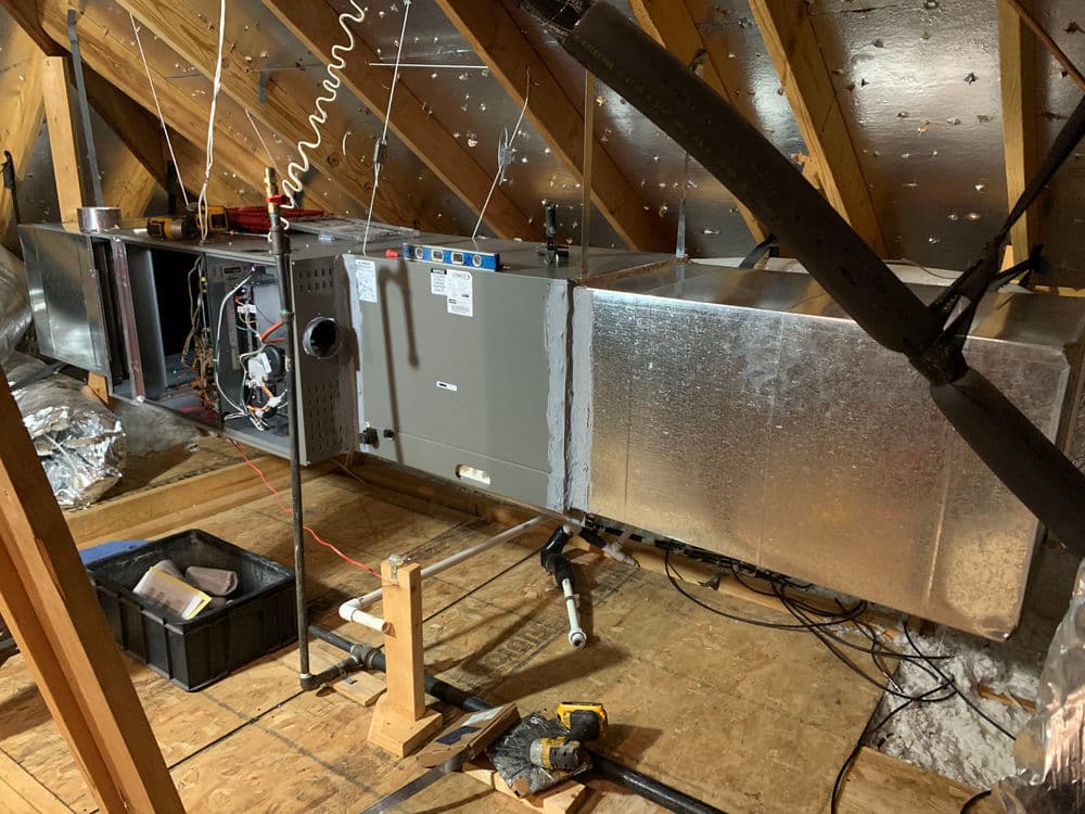 HVAC unit and ductwork installation in an attic with insulation and tools visible.